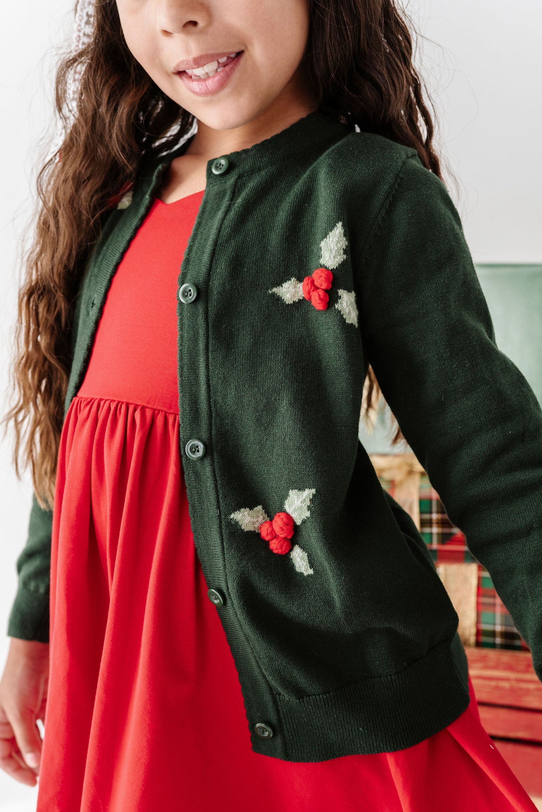 girl wearing 3d holly knit cardigan over red dress for christmas