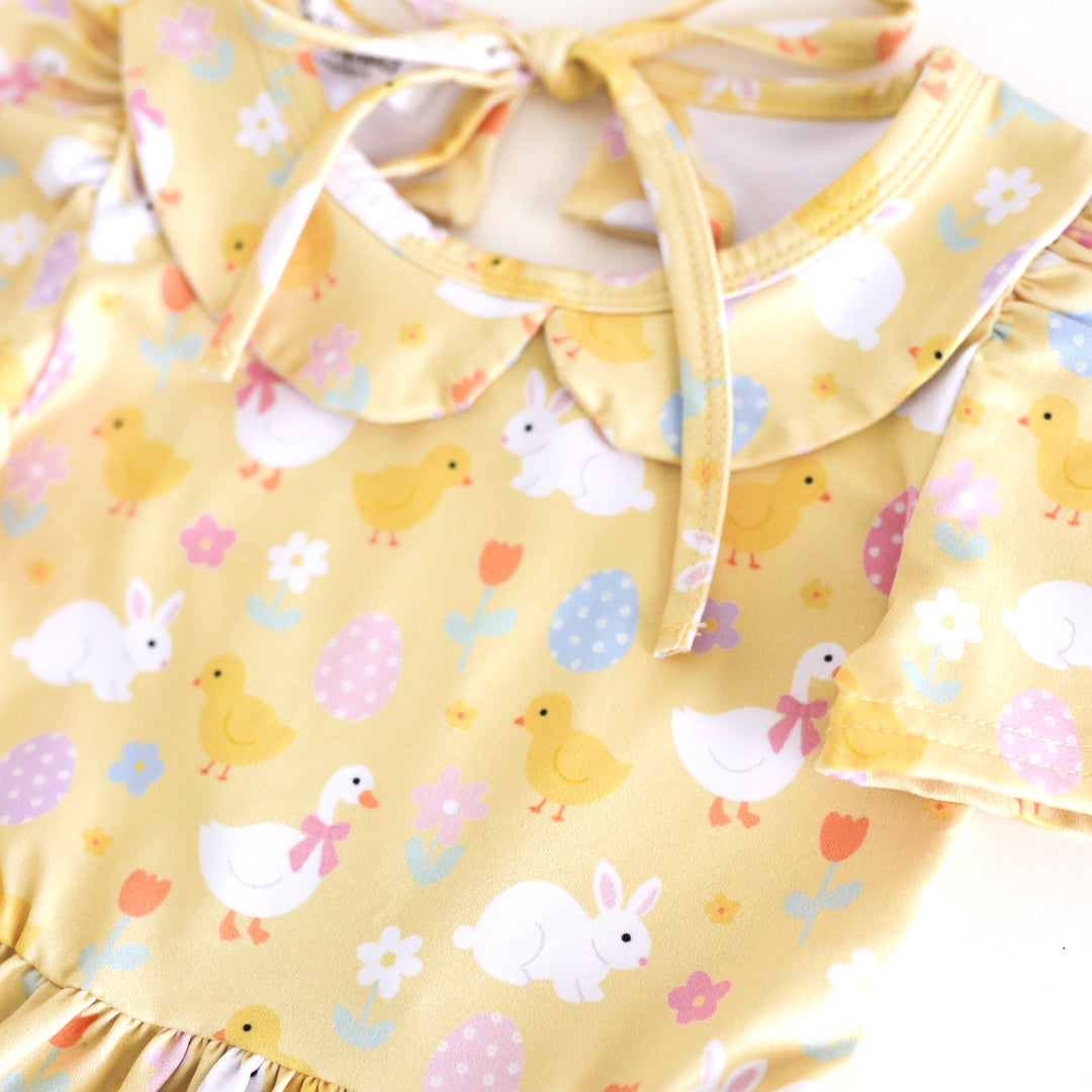 closeup of girls' pastel yellow twirl dress with peter pan collar and Easter print featuring bunnies, chicks, geese, flowers and Easter eggs