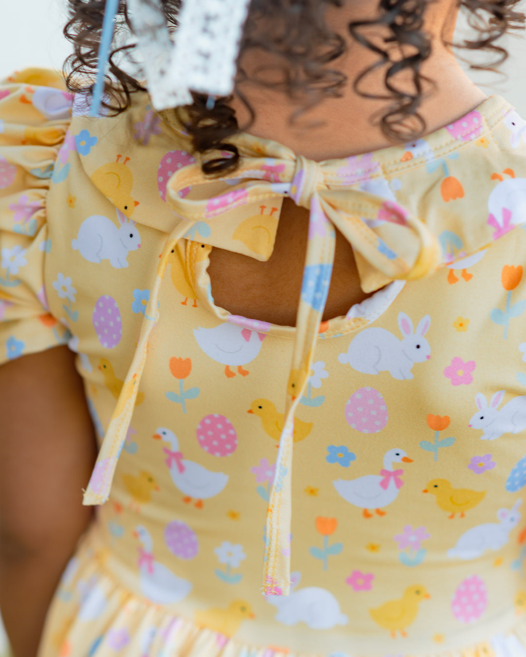 closeup of tie back on little girls yellow Easter themed twirl dress with bunnies, geese and chicks