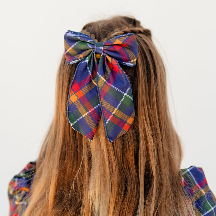 girl wearing oversized double fabric bow in navy plaid print with matching twirl dress for back to school