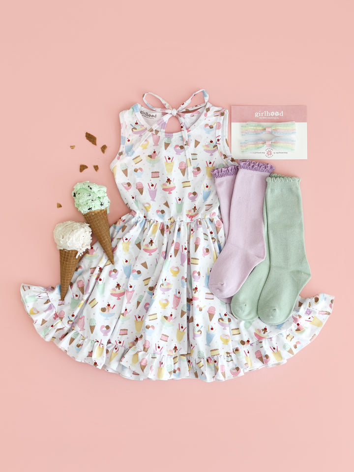 flatlay of sleeveless twirl dress in white with pastel ice cream print and matching lilac and mint colored knee high socks and pastel pigtail bows