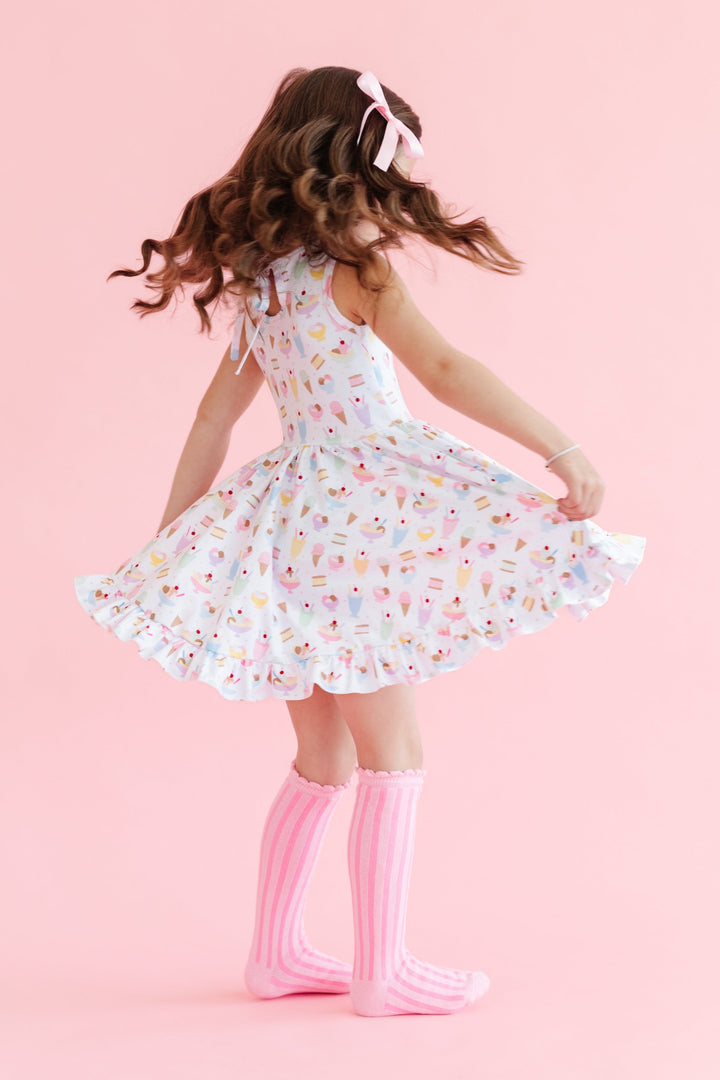 girl spinning in sleeveless twirl dress in white with pastel ice cream print and matching pink striped knee highs and satin ribbon bow