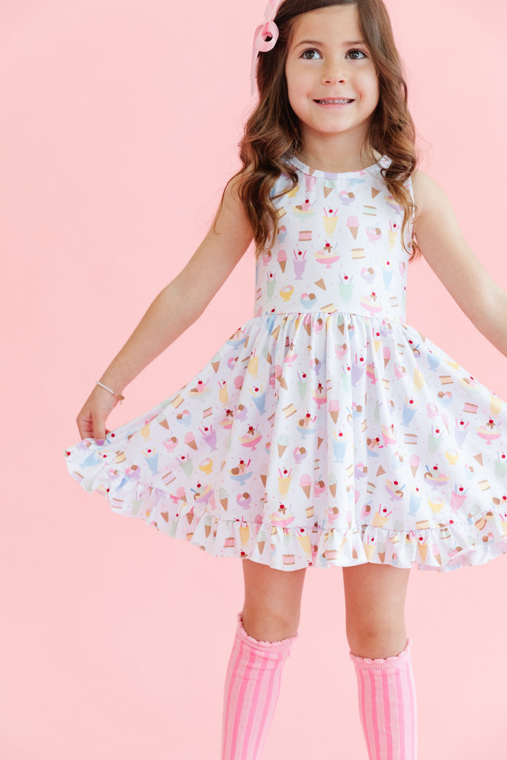 girl wearing sleeveless twirl dress in white with pastel ice cream print and matching pink striped knee highs and satin ribbon bow