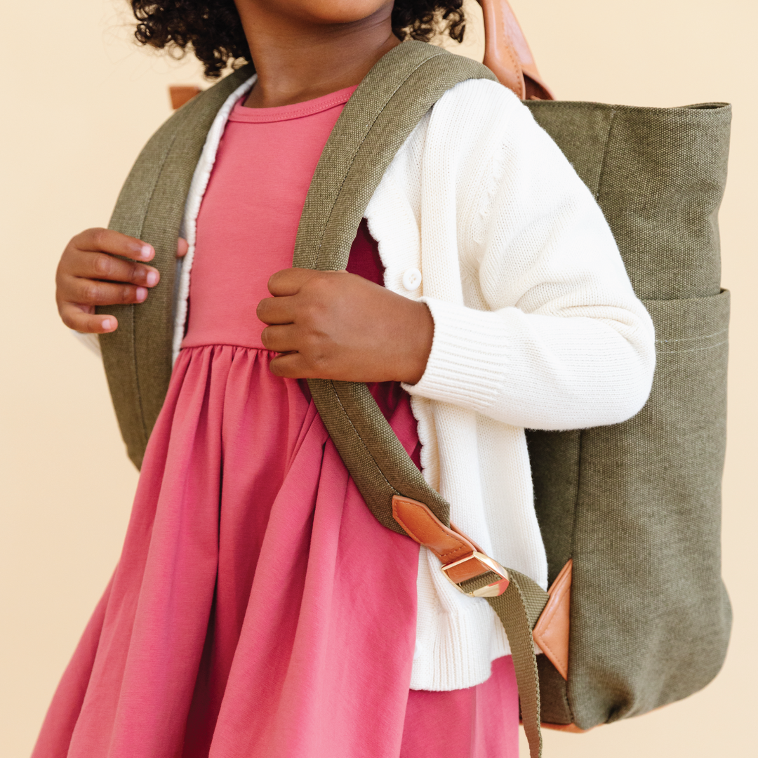 little girl in pink dress wiht ivory cardigan and green backpack