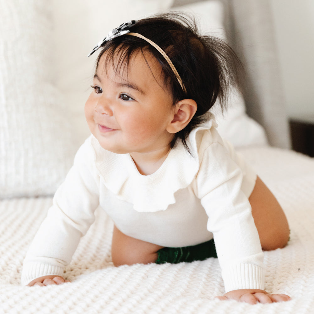 baby girl wearing cream sweater romper and knee high socks crawling on bed