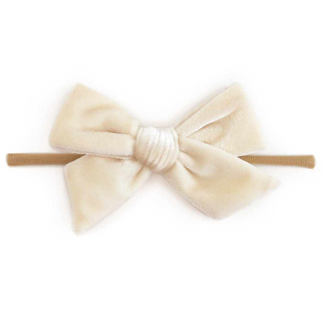 A cream-colored velvet bow headband with a textured white center and a tan elastic band, shown against a plain white background.