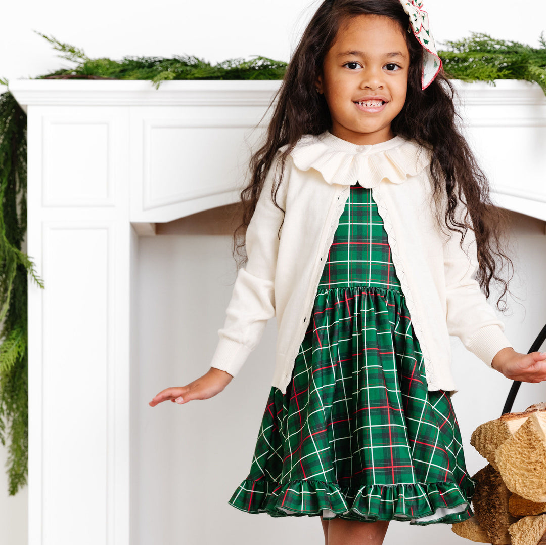 little girl posing in green christmas plaid twirl dress and ivory ruffle cardigan