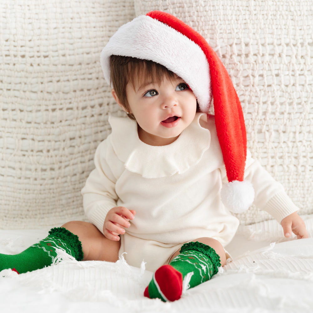 adorable baby girl wearing cream sweater romper, santa hat and green christmas knee high socks