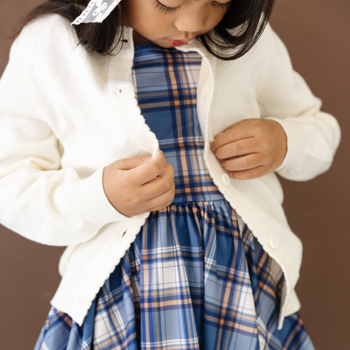little girl in blue plaid twirl dress and creamy white button front cardigan with scalloped trim for fall