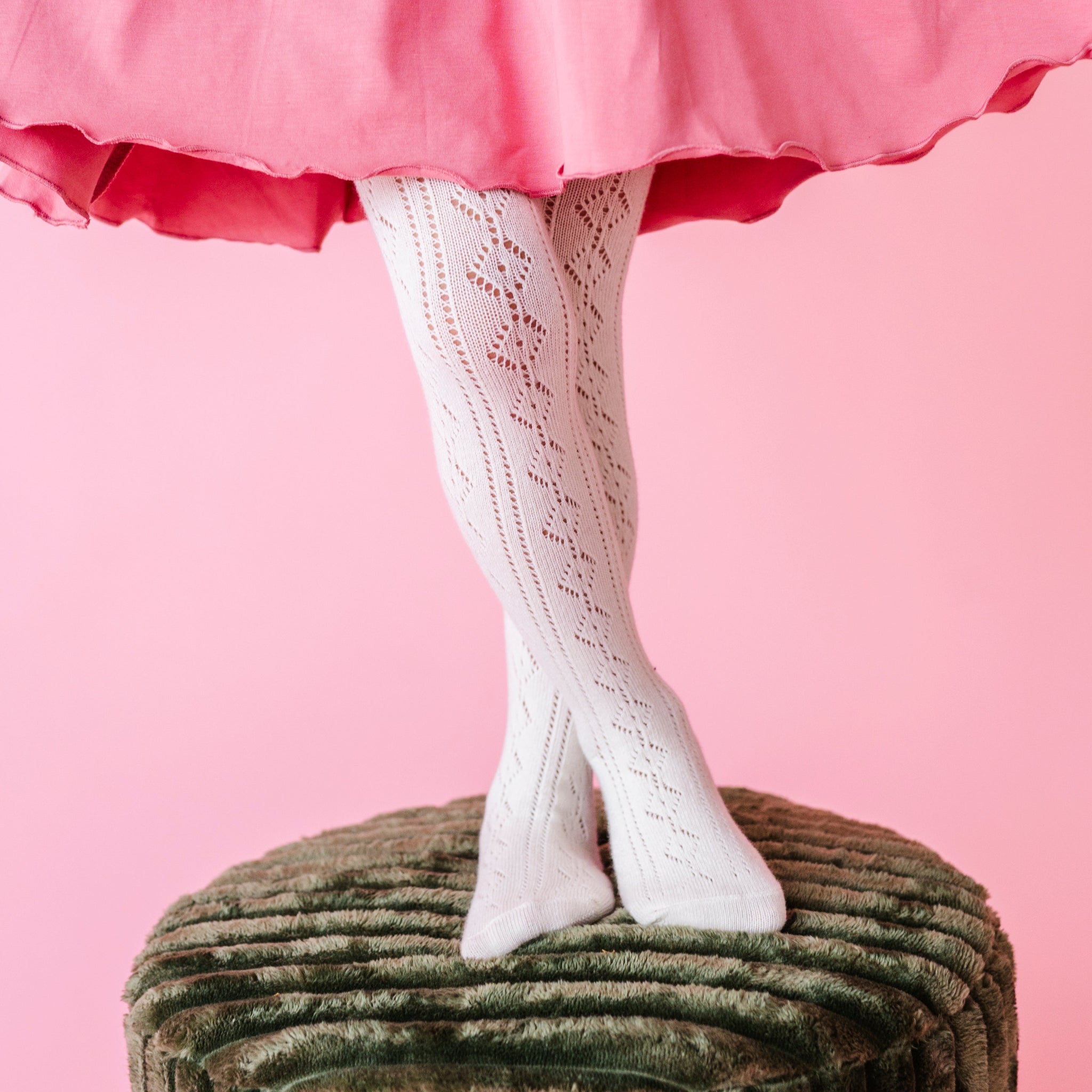 closeup of little girl standing on green velvet stool in ivory pointelle tights paired with pink lettuce trim twirl dress