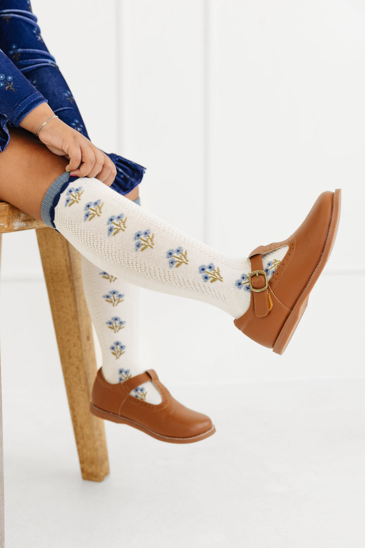 little girl in brown mary janes and light cream knee highs with petite blue flower bouquet pattern and blue trim to match fall outfits