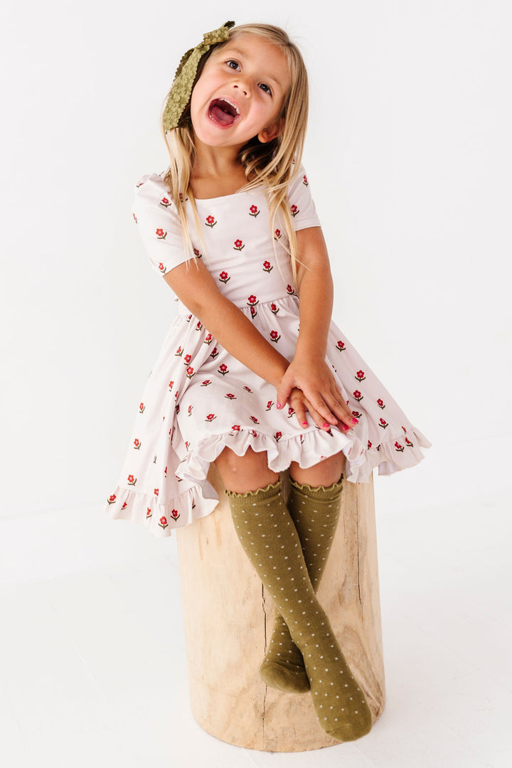 little girl sitting on stool wearing ivory flower print dress with coordinating olive green dotted knee high socks