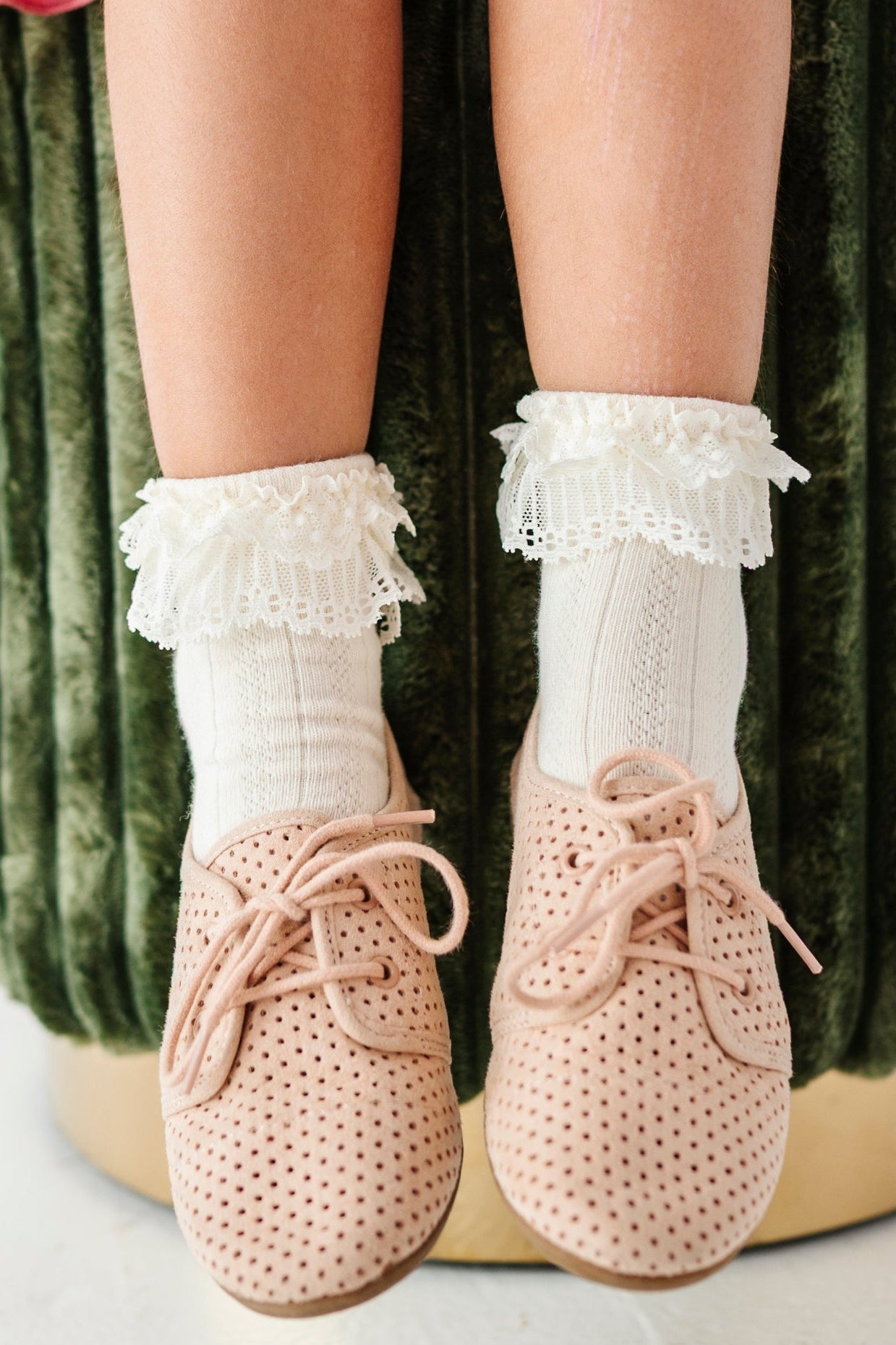 little girl sitting on green velvet stool wearing ivory ankle socks with lace trim and cream oxford shoes