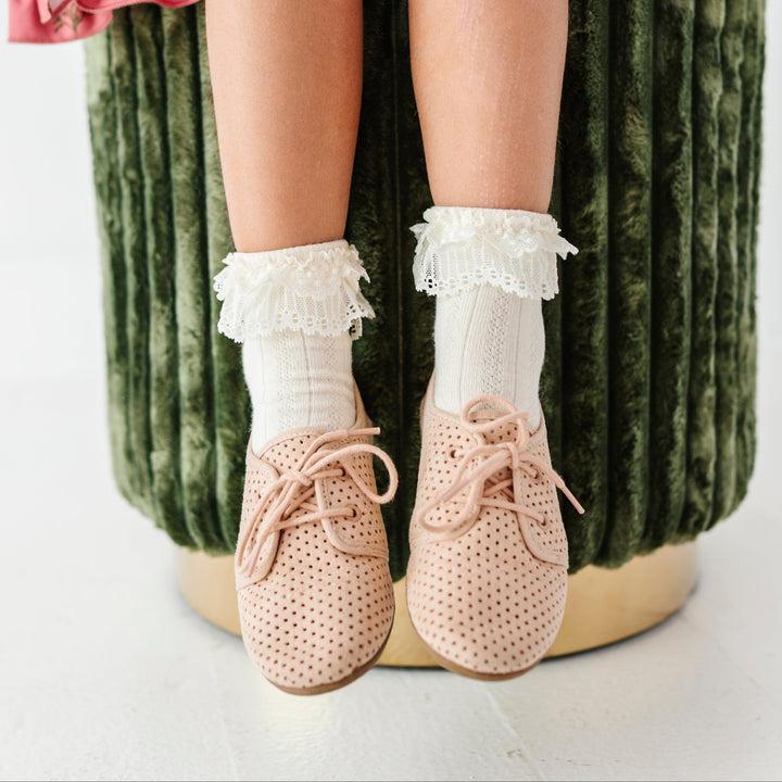 little girl sitting on green velvet stool wearing ivory ankle socks with lace trim and cream oxford shoes