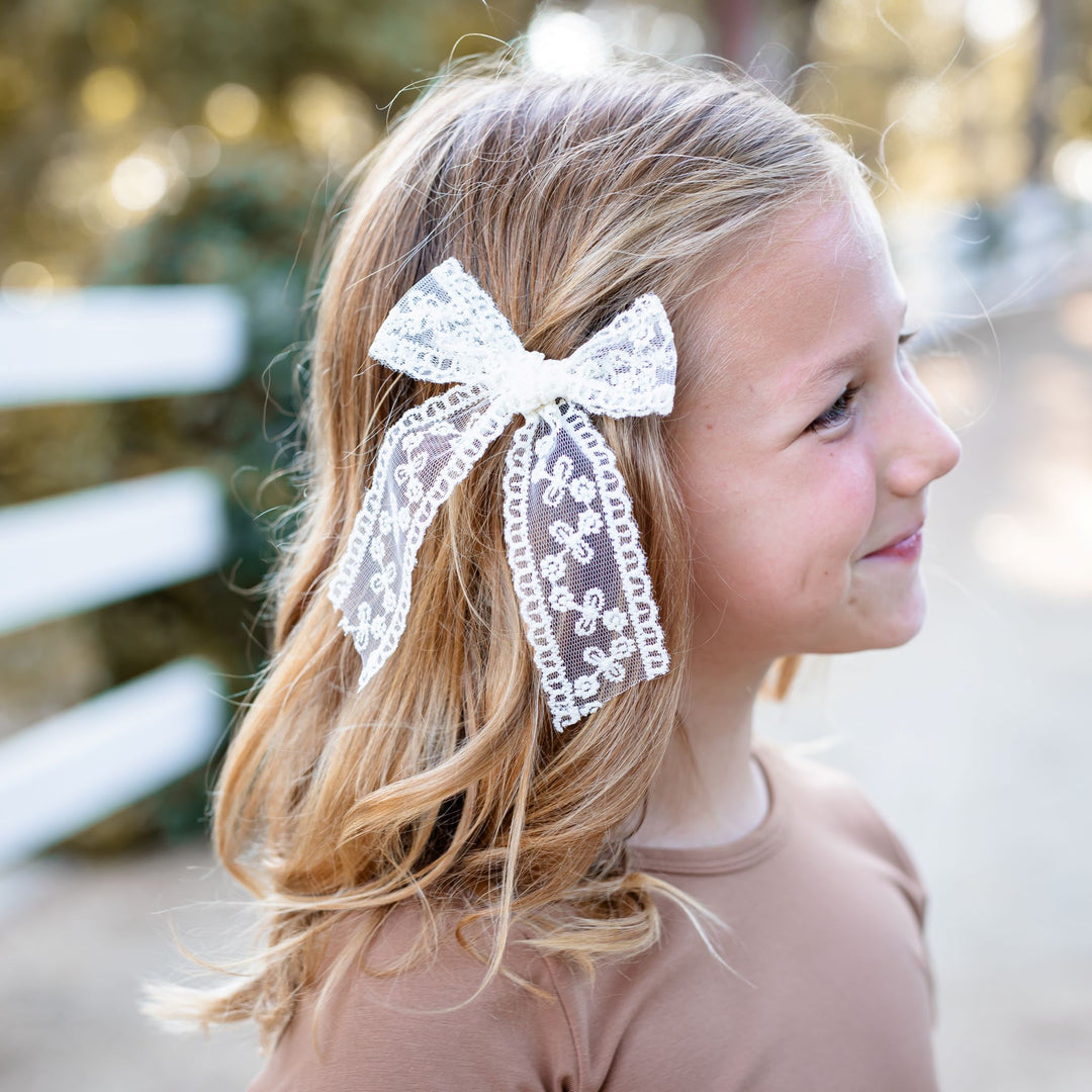 little girl in neutral dress and matching cream colored lace bow