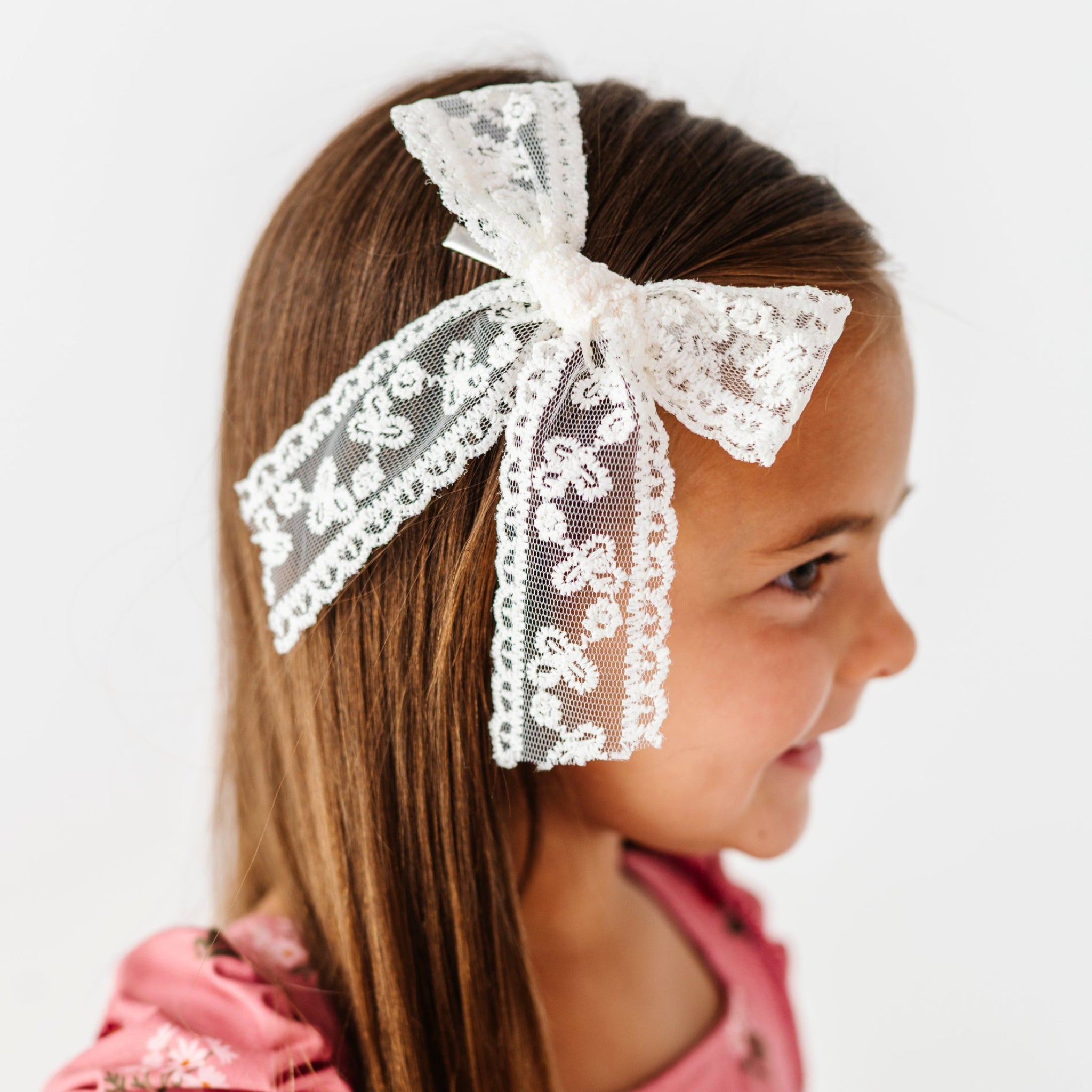 young girl in ivory lace hair bow on alligator clip paired with pink twirl dress with ivory floral print