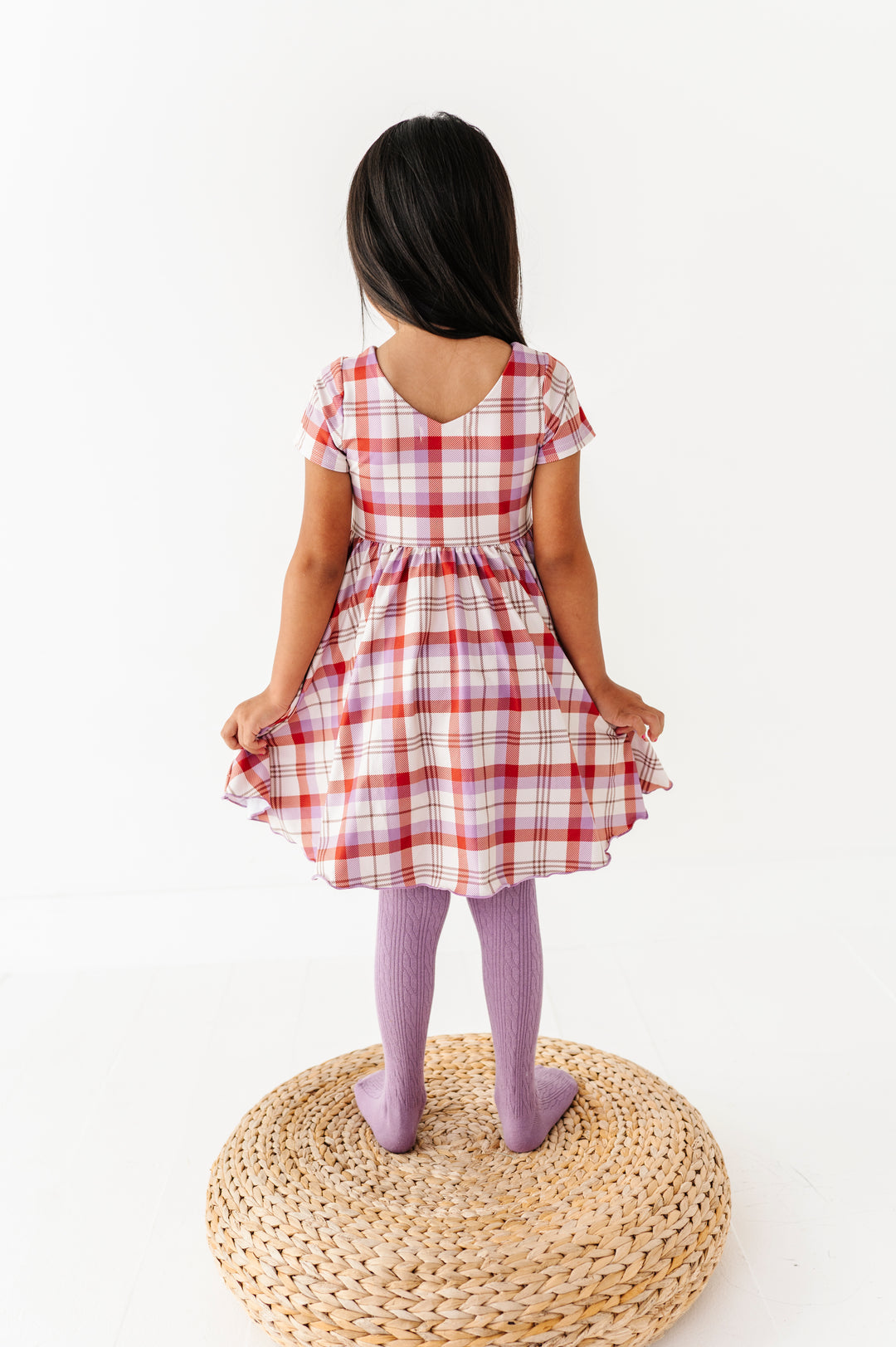 back view of little girl in v-neck ivory plaid twirl dress paired with matching amethyst cable knit tights
