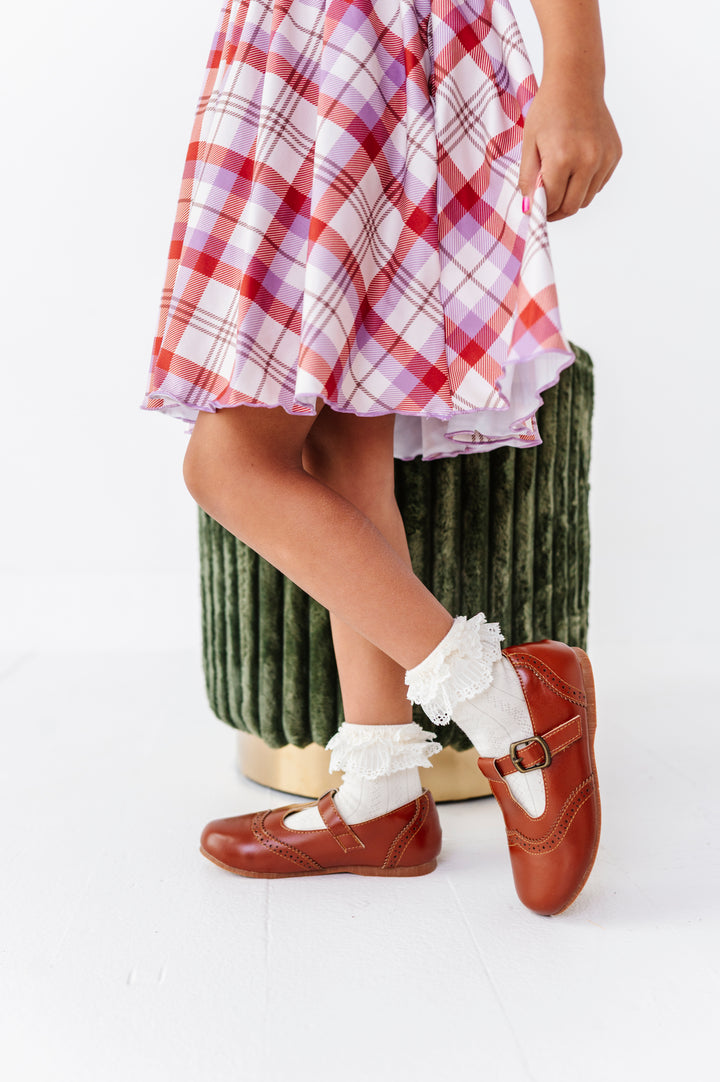 closeup of little girl wearing light cream lace top bobby socks paired with brown mary janes and ivory, rust and purple plaid twirl dress
