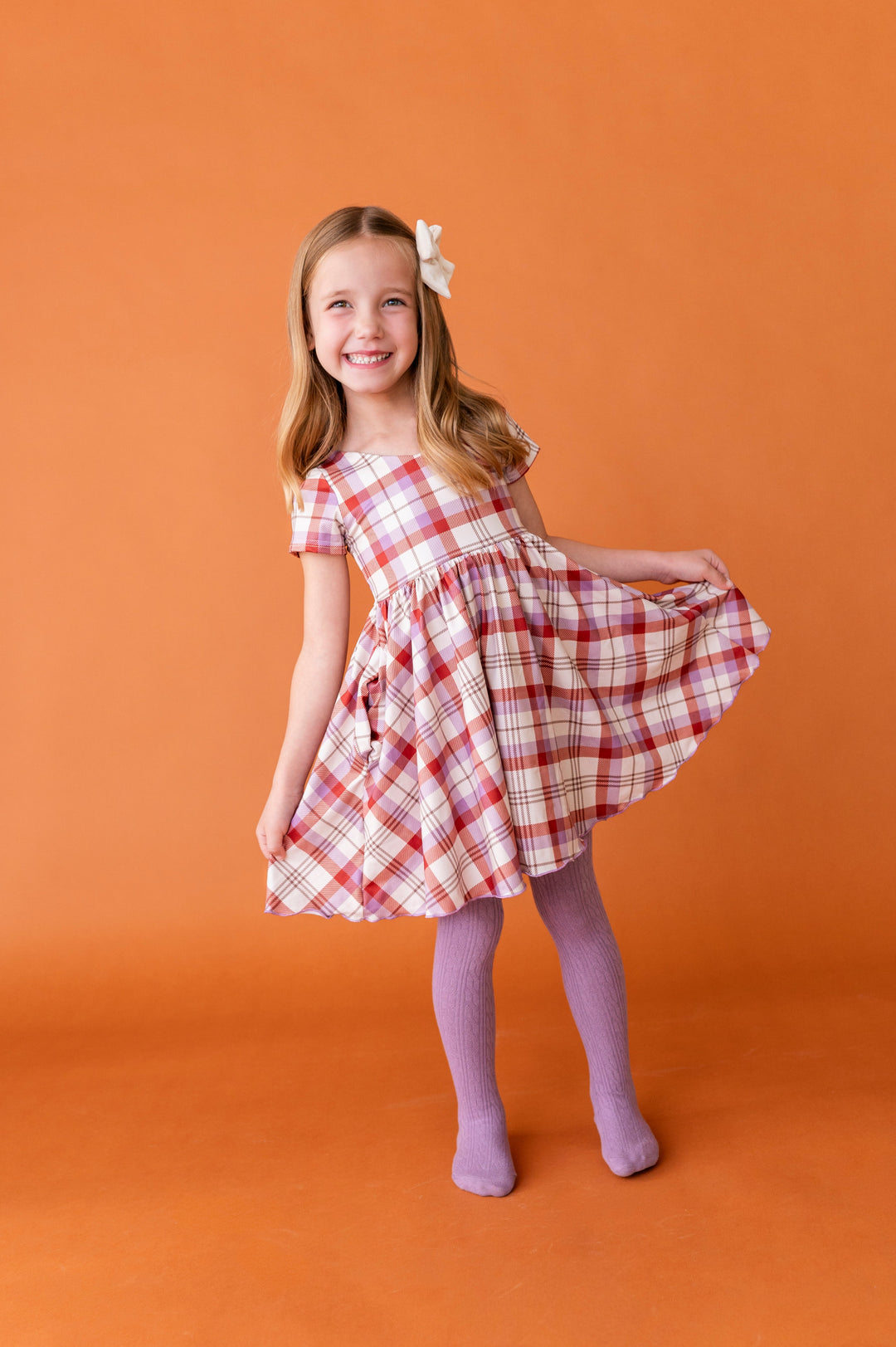 young girl in ivory, rust and purple plaid twirl dress paired with matching purple cable knit tights