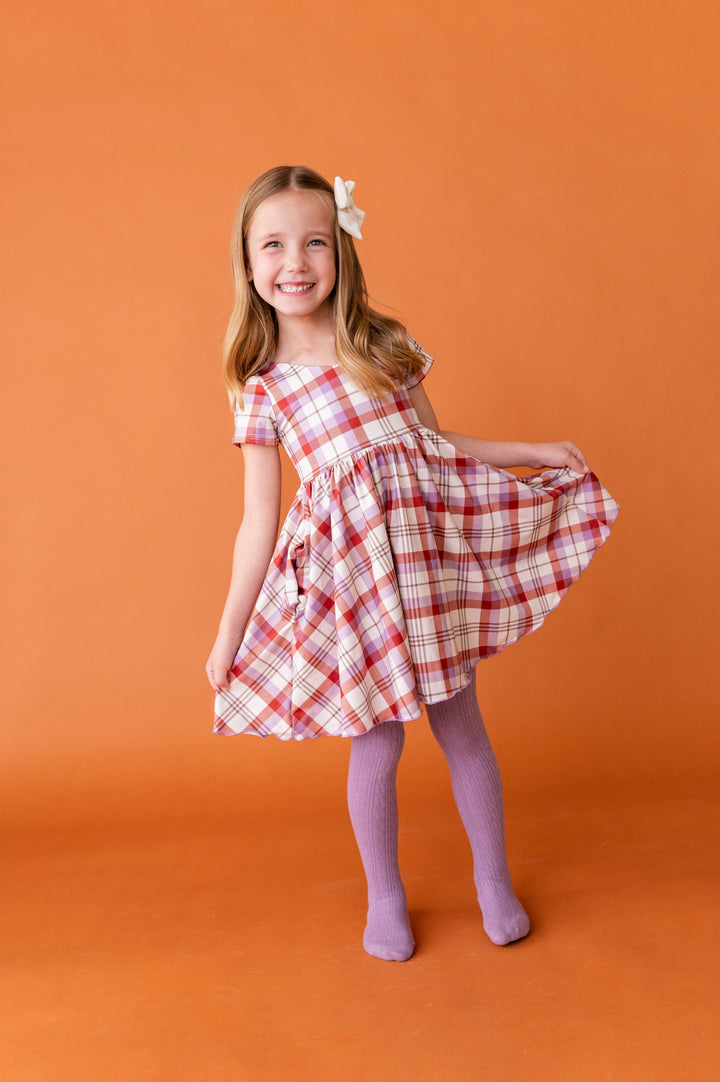 young girl in ivory, rust and purple plaid twirl dress paired with matching purple cable knit tights