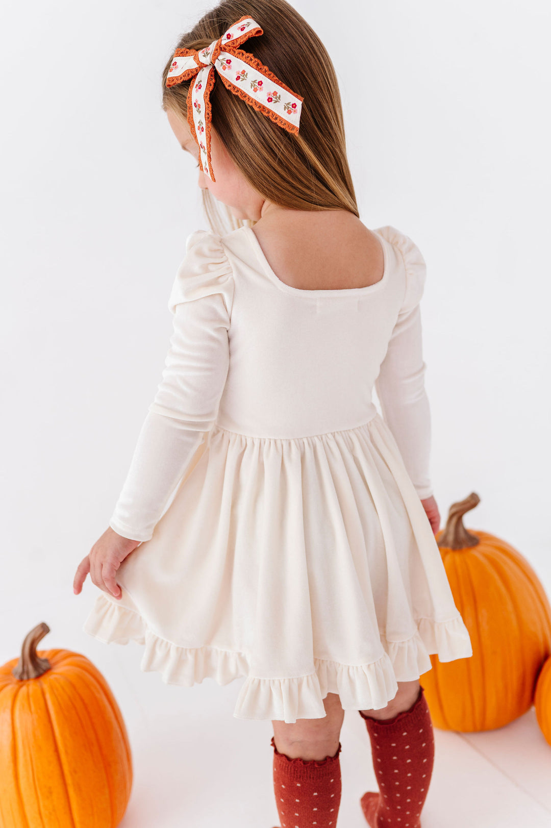little girl wearing ivory dress with rust colored hair bow and knee high socks
