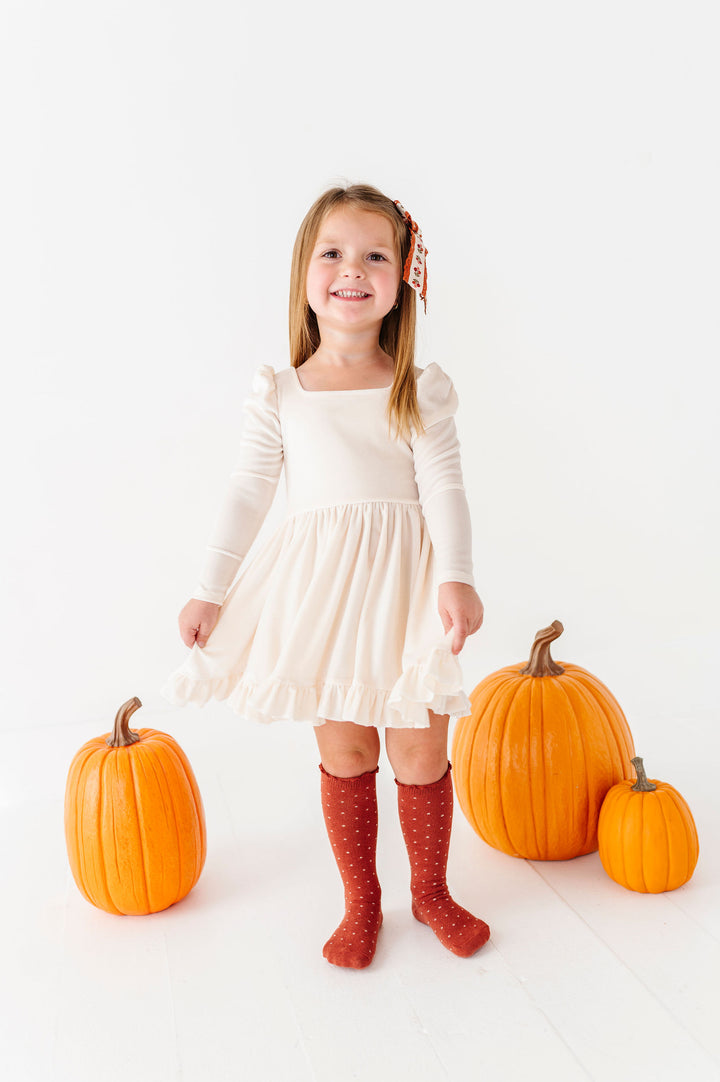 girl wearing ivory velvet dress with rust polka dot knee high socks standing with pumpkins