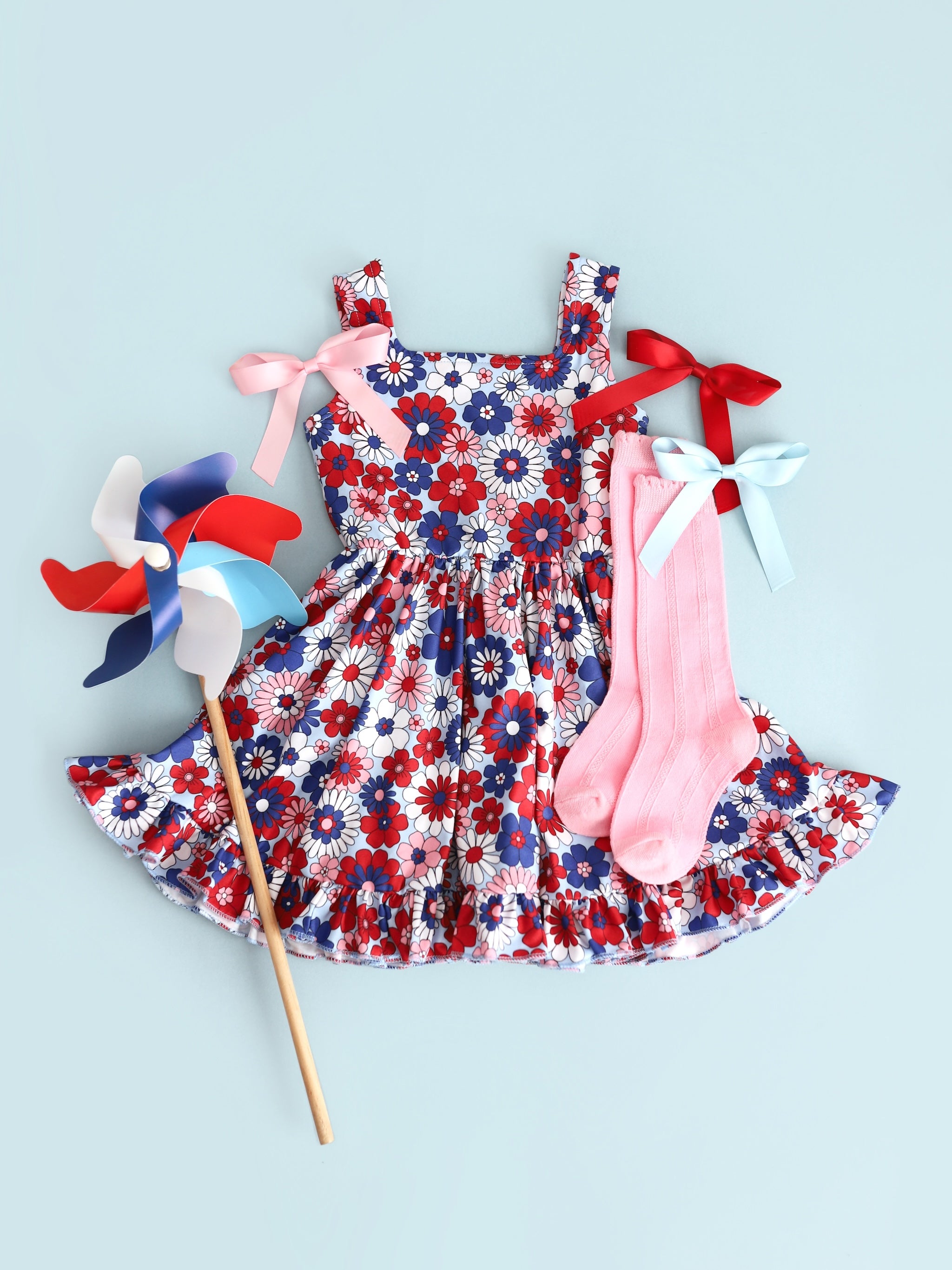 flatlay of girls floral 4th of july summer twirl dress with matching pink scallop knee highs and satin hairbows