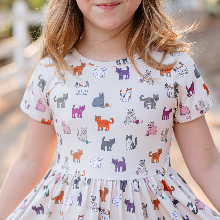 closeup of girls short sleeve twirl dress in cream with orange, grey, purple and white cat print