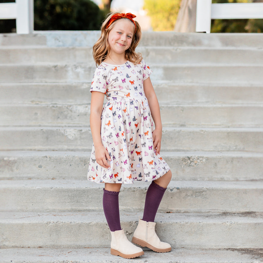 little girl in cream fall twirl dress with playful kitten print and matching purple knee highs and pumpkin spice velvet headband