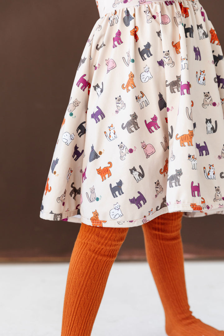 little girl in cat print twirl dress and matching fall orange cable knit tights