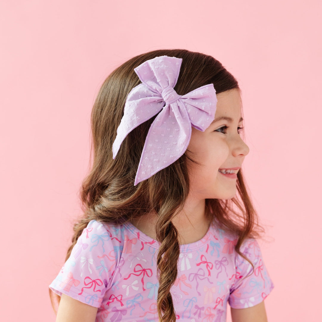 girl wearing lavender purple party girl bow with raised dot texture and matching purple twirl dress with bows printed on it