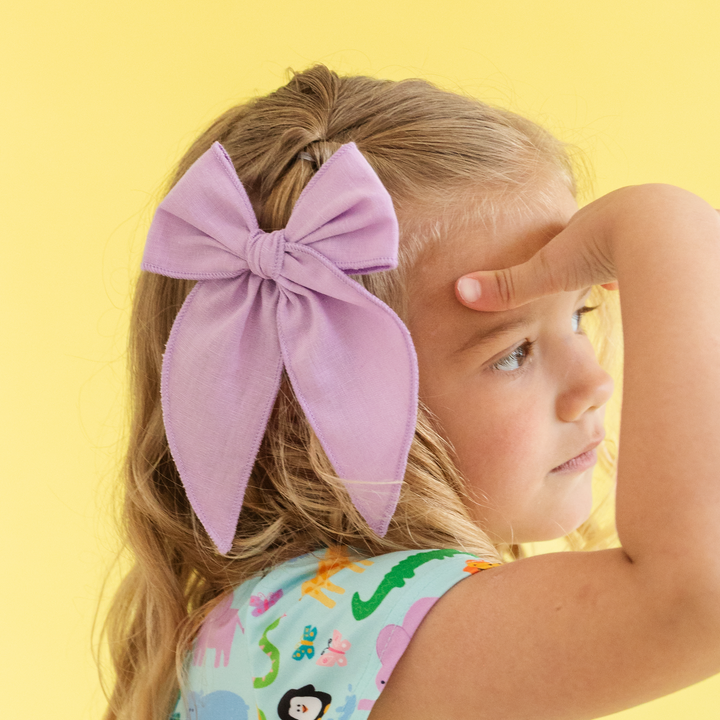 girl wearing light purple hair bow on alligator clip in front of yellow background wearing blue zoo animal dress