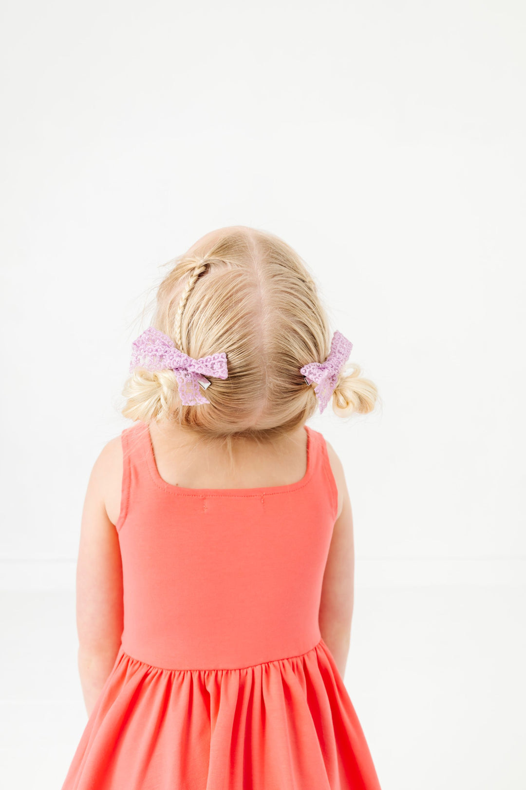 little girl with pastel purple lace pigtail bows on clip and coral sleeveless twirl dress