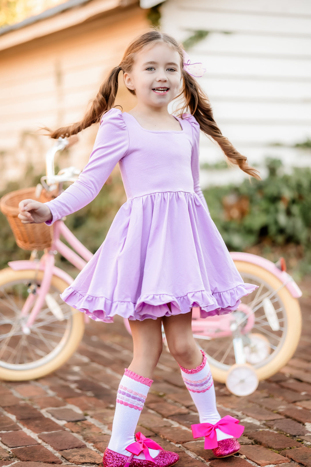 girl twirling in front of pink bicycle in light purple cotton blend long sleeve twirl dress with pastel bubble stripe knee highs and sparkly pink shoes 