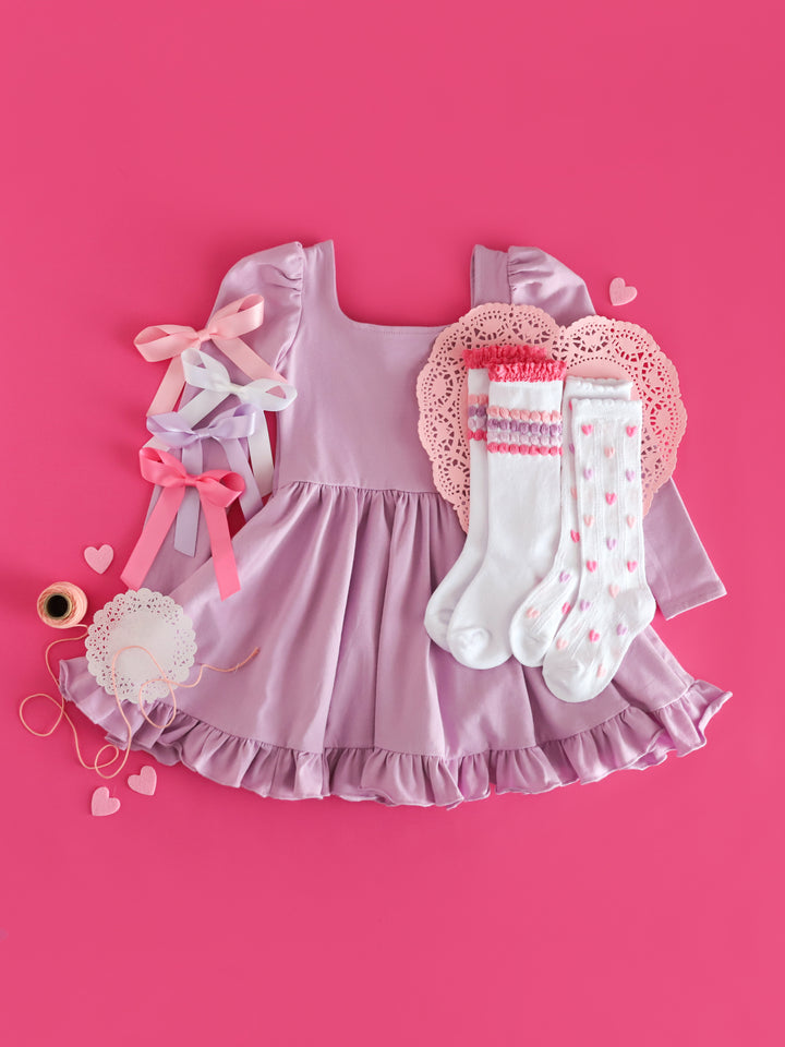 girls' lavender long sleeve twirl dress with made to match satin ribbon hair bows and pastel knee high socks on doilies for Valentine's Day