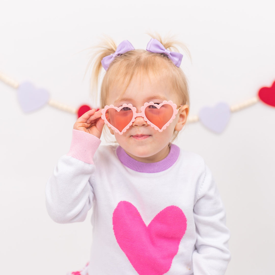 little girl in valentine's sweater with pink heart wearing heart sunnies and lavender satin pigtail bows on clips