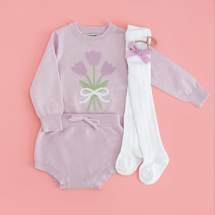 baby girls' spring outfit flat lay with light purple tulip sweater and matching baby knit bloomers paired with white cable knit tights and purple lace baby bow