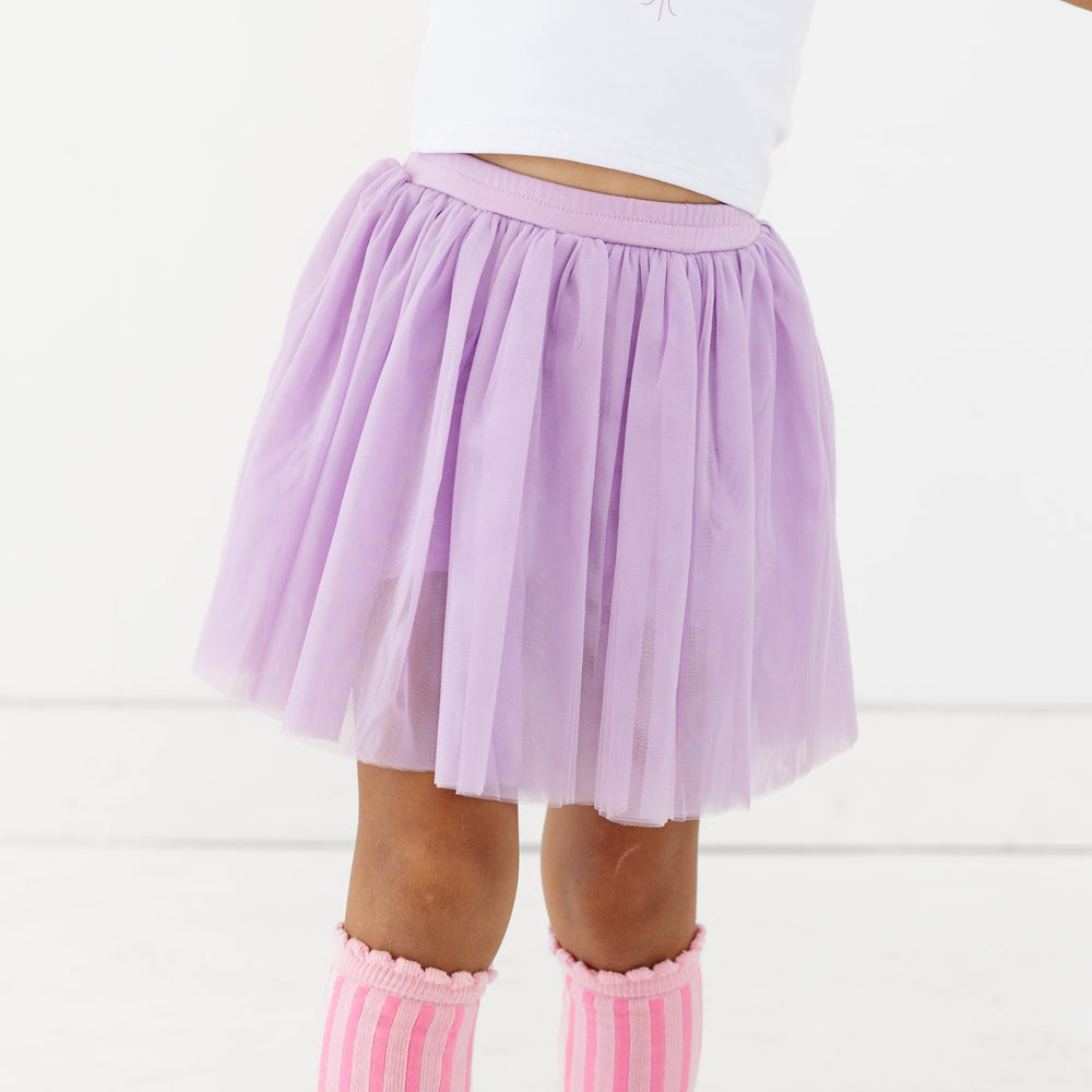 closeup of little girl in lavender tulle skirt with attached shorts and scallop trimmed pink striped knee high socks