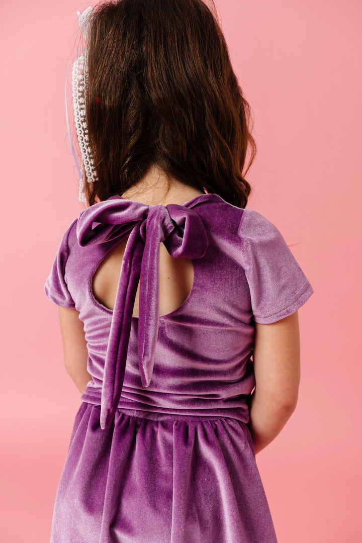back view of little girl in purple velvet top with large keyhole and oversized velvet bow closure paired with matching velvet skort for valentines day