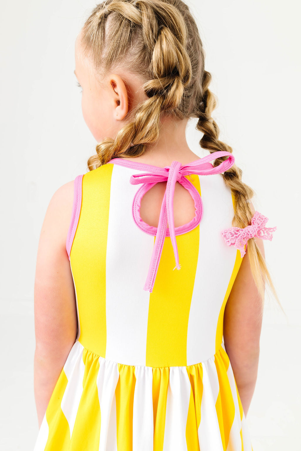 close up of girl in pink trimmed keyhole tie back on yellow and white striped summer twirl dress