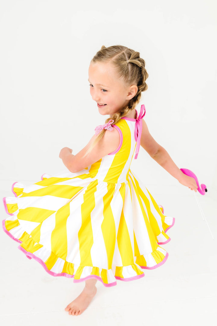 little girl twirling in yellow and white wide striped sleeveless twirl dress with pink trim 