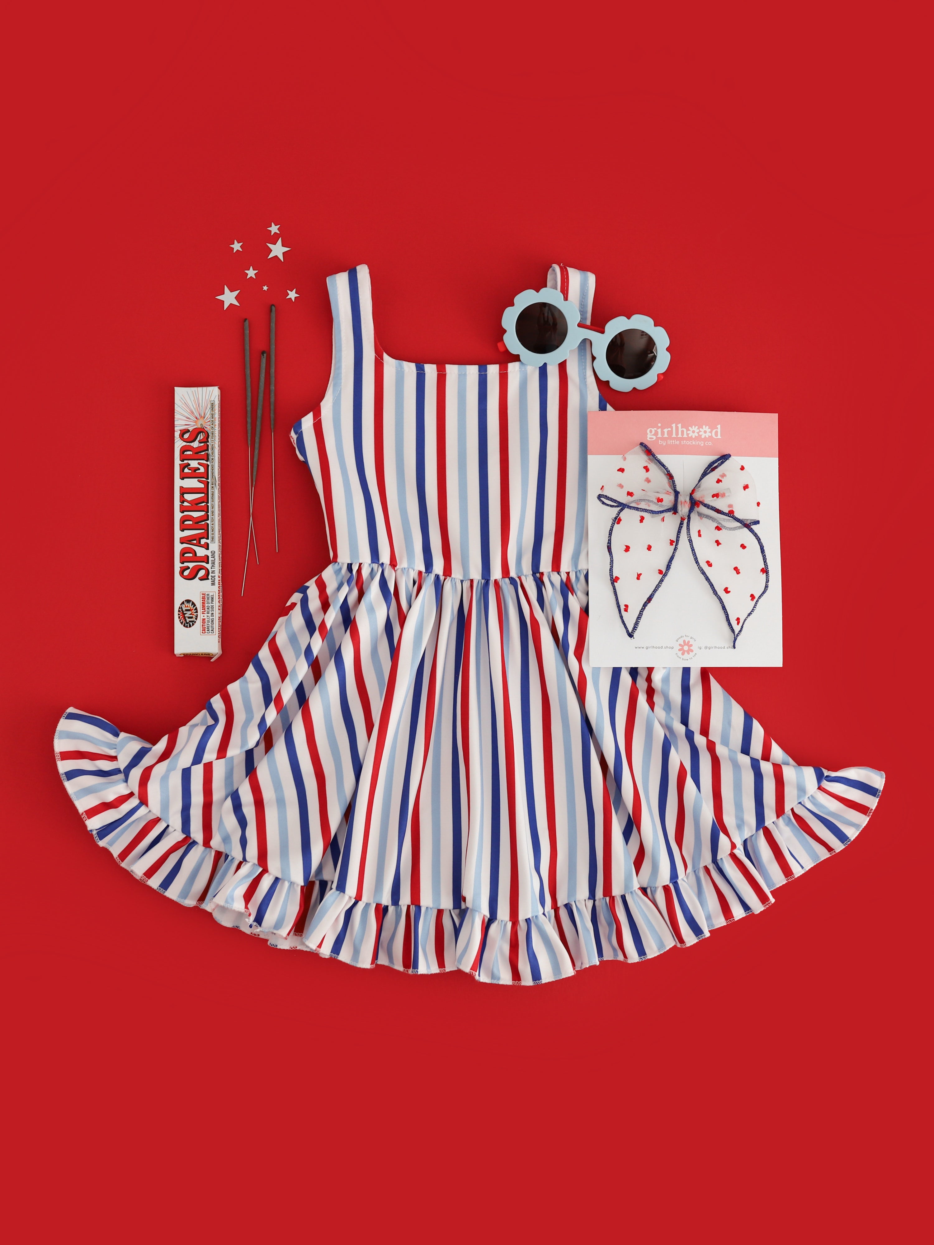 girls red, white and blue vertical striped sleeveless twirl dress styled for the 4th of July with sparklers, matching bow and sunnies