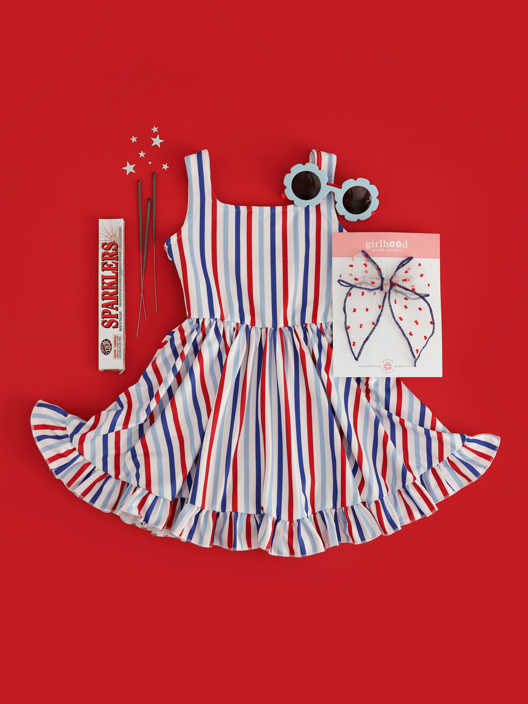 girls red, white and blue vertical striped sleeveless twirl dress styled for the 4th of July with sparklers, matching bow and sunnies