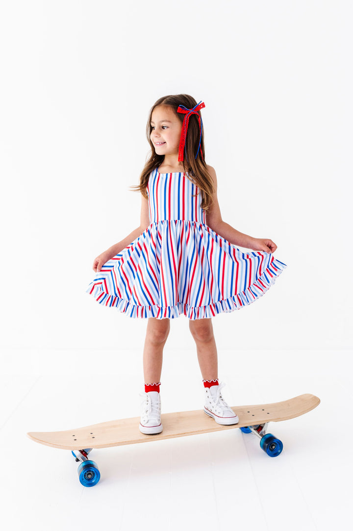 little girl on skateboard in red, white and blue striped sleeveless twirl dress paired with red lace/blue ribbon bow, red lettuce trim midi socks and white high tops