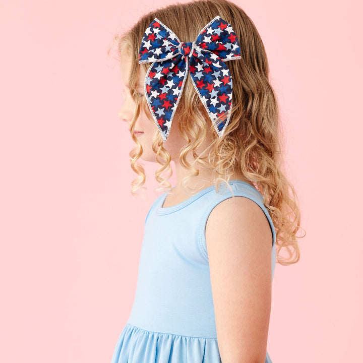 little girl turned to side in light blue summer dress and matching 4th of july hair bow