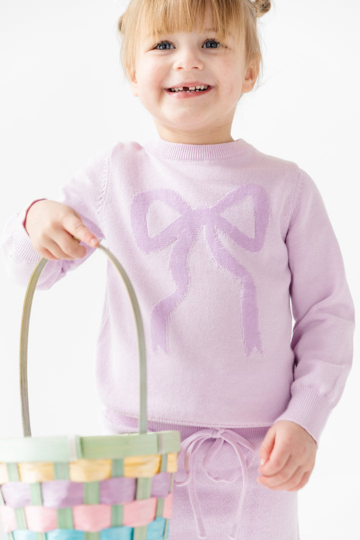 girl wearing light purple cotton knit pullover sweater with purple bow design and matching skirt holding an easter basket