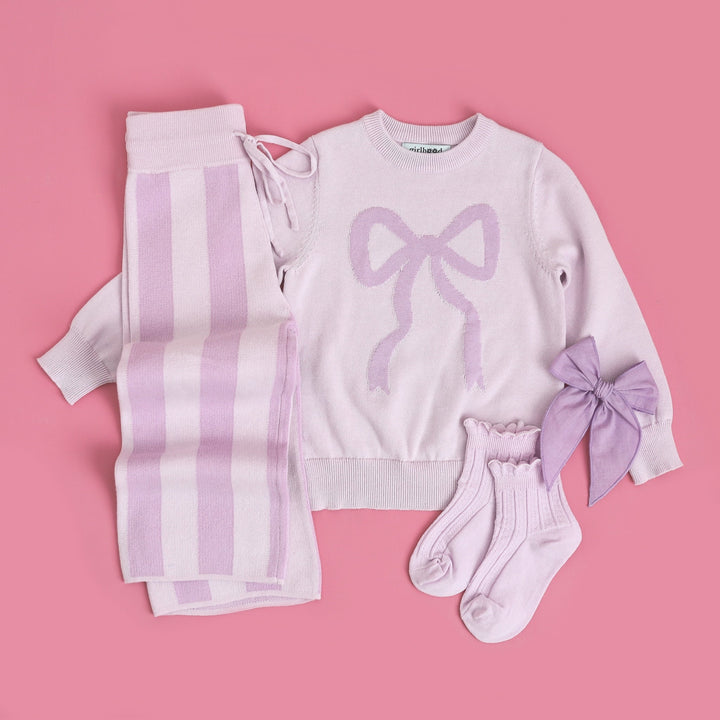 flatlay of girls spring outfit with lilac and lavender stripe cotton knit pants and matching sweater with bow on it and matching socks and hairbow