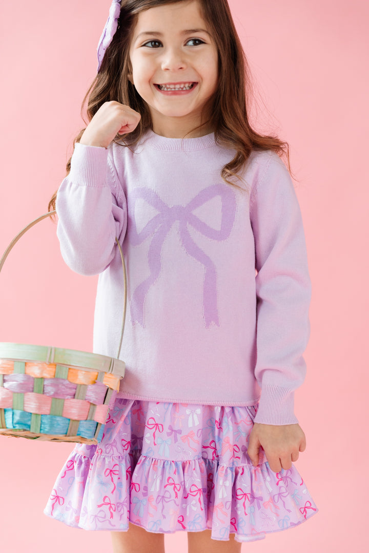 girl wearing light purple cotton knit pullover sweater with purple bow design and matching bow print dress holding easter basket