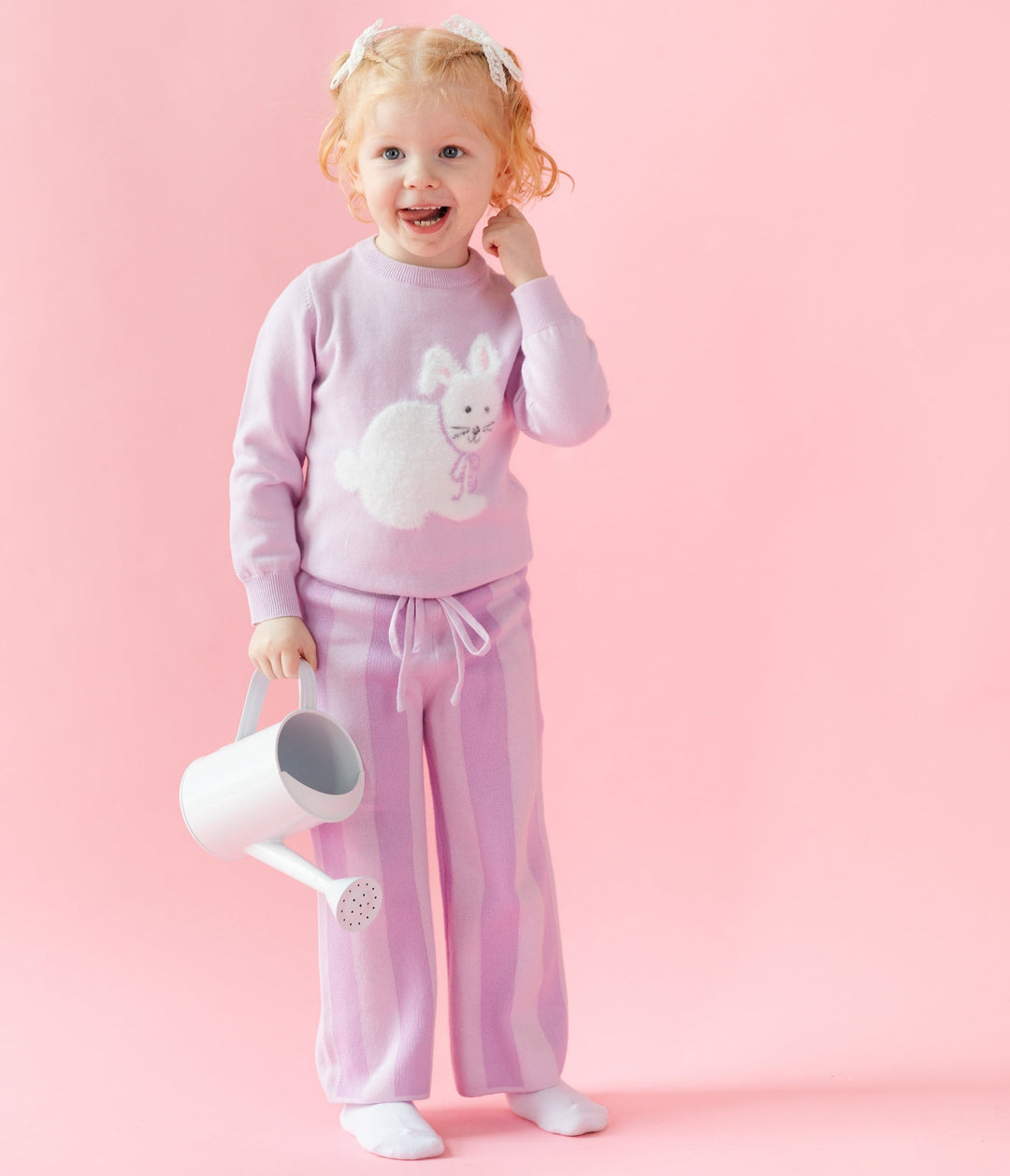 little girl with watering can in purple striped cotton knit pants and pullover sweater that is lilac with a fuzzy white bunny on it