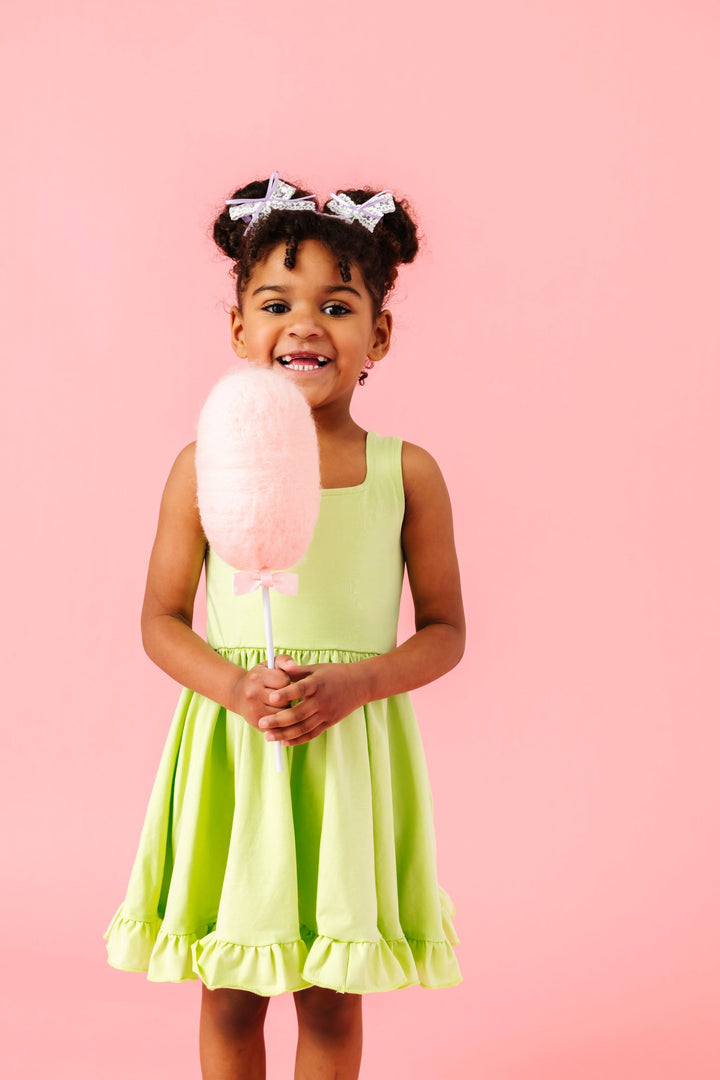 little girl holding cotton candy in lime green sleeveless twirl dress paired with white lace and lavender ribbon pigtail bows